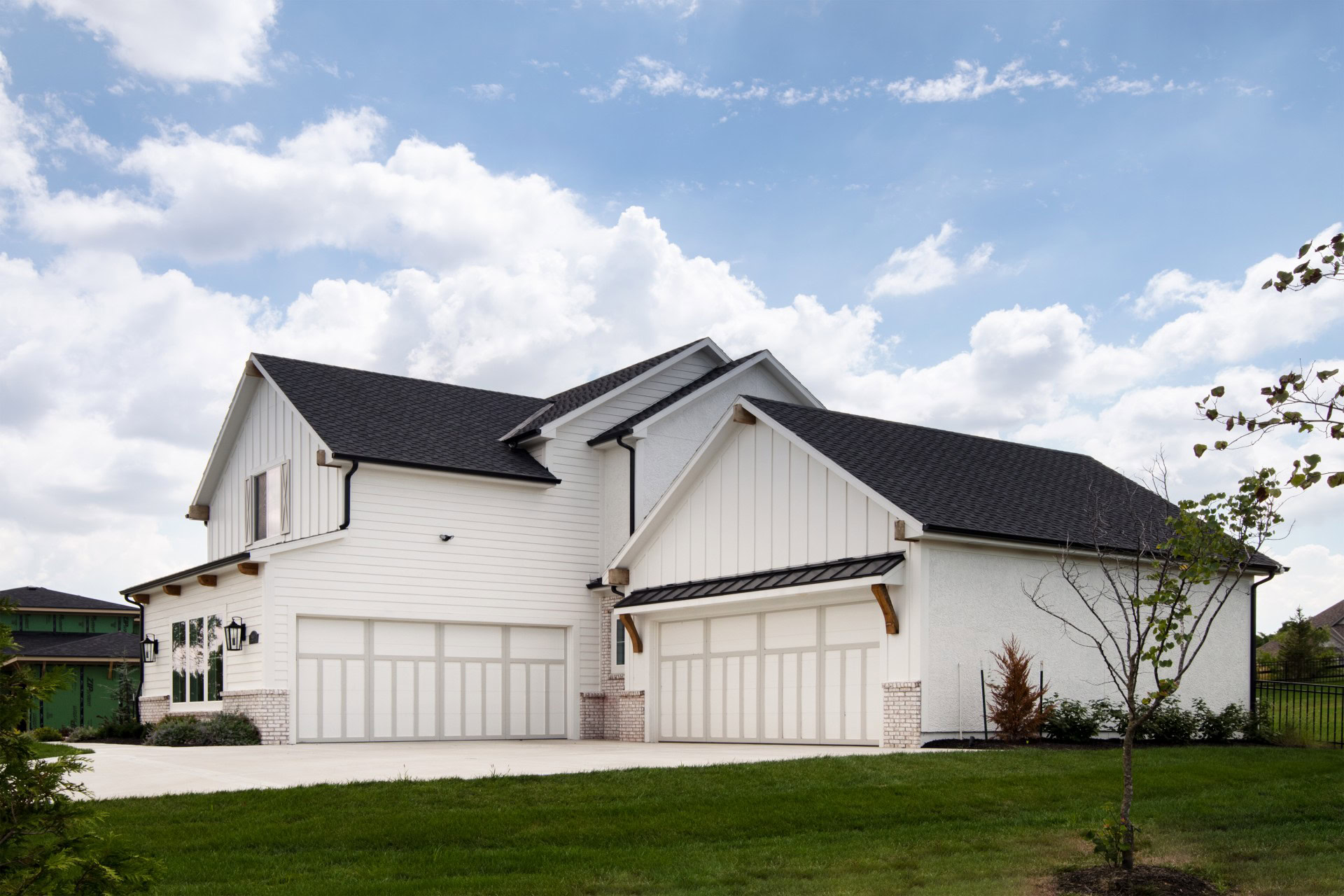 Modern White Farmhouse with Black Roof Beautiful white farmhouse with black roofing and spacious garage, set against a bright blue sky with.